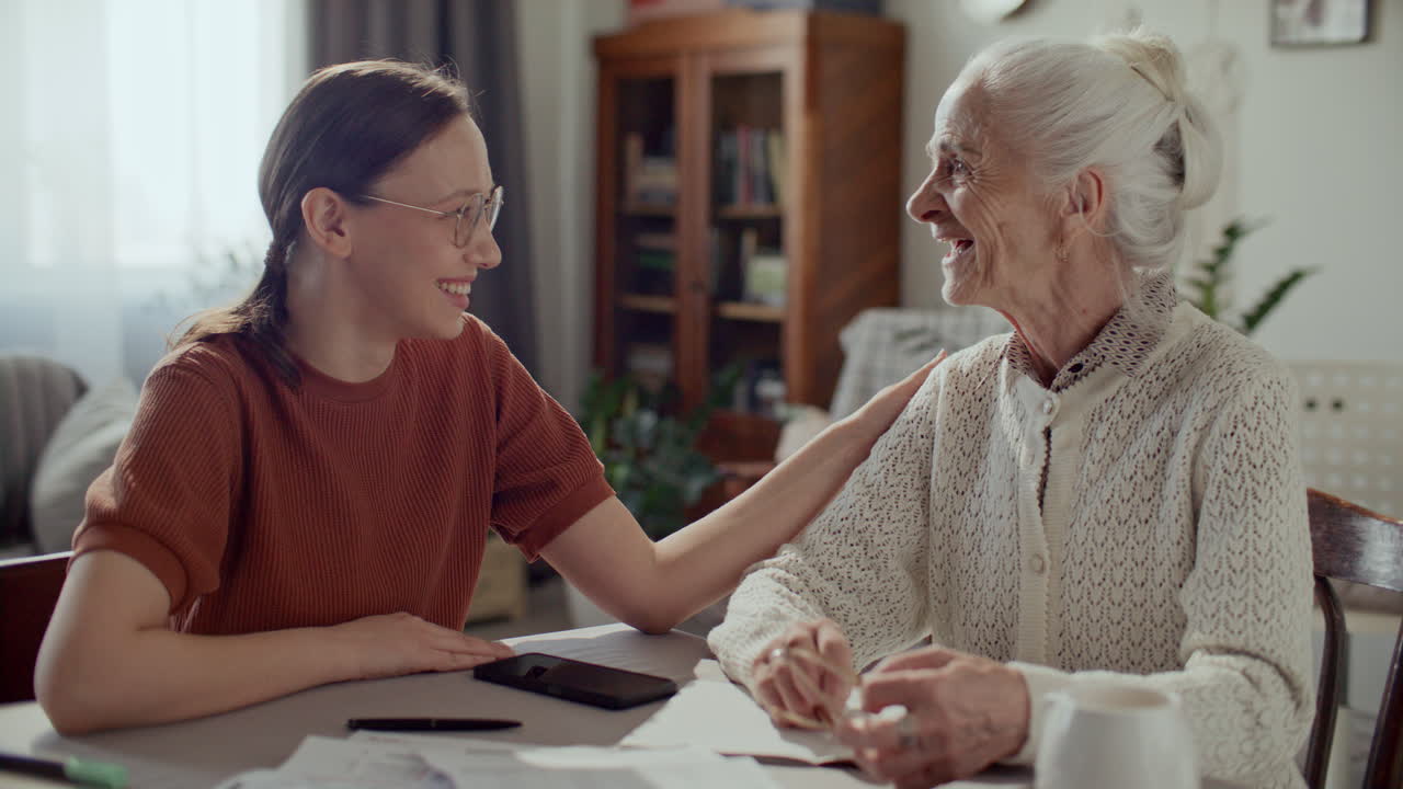 Young Woman Supporting Elderly Grandmother during Paperwork at Home