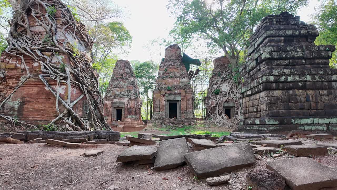 Wide shot frames all five stone towers of Prasat Bram, temple ruins glowing as sunlight filters through, casting a warm, golden glow over the ancient site.