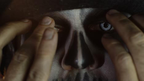 rostro de hombre de primer plano en esqueleto cosplay de halloween quitando las manos de la cara y mirando con los ojos bien abiertos