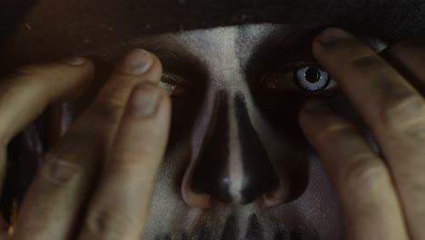 close-up man face in skeleton halloween cosplay removing hands from face and looking wide open eyes