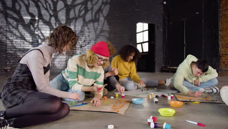 Young-environmental-activists-painting-placards-sitting-on-the-floor