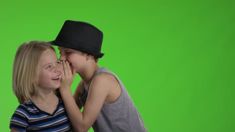 older brother whispers something to younger brother in front of greenscreen