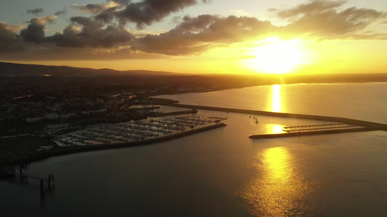 Dun Laoghaire Harbour, April 2020, Dublin, Ireland. Drone slowly pulls backward away from Marina, revealing views of East and West Piers with a spectacular golden sunset in the distance.