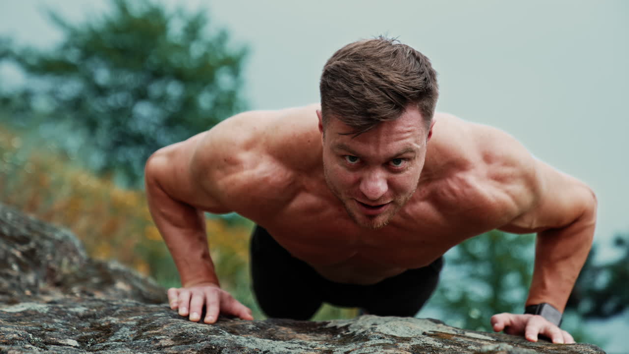 Front view of a strong man standing in plank. Athlete doing pushups on the rock. Blurred nature backdrop.
