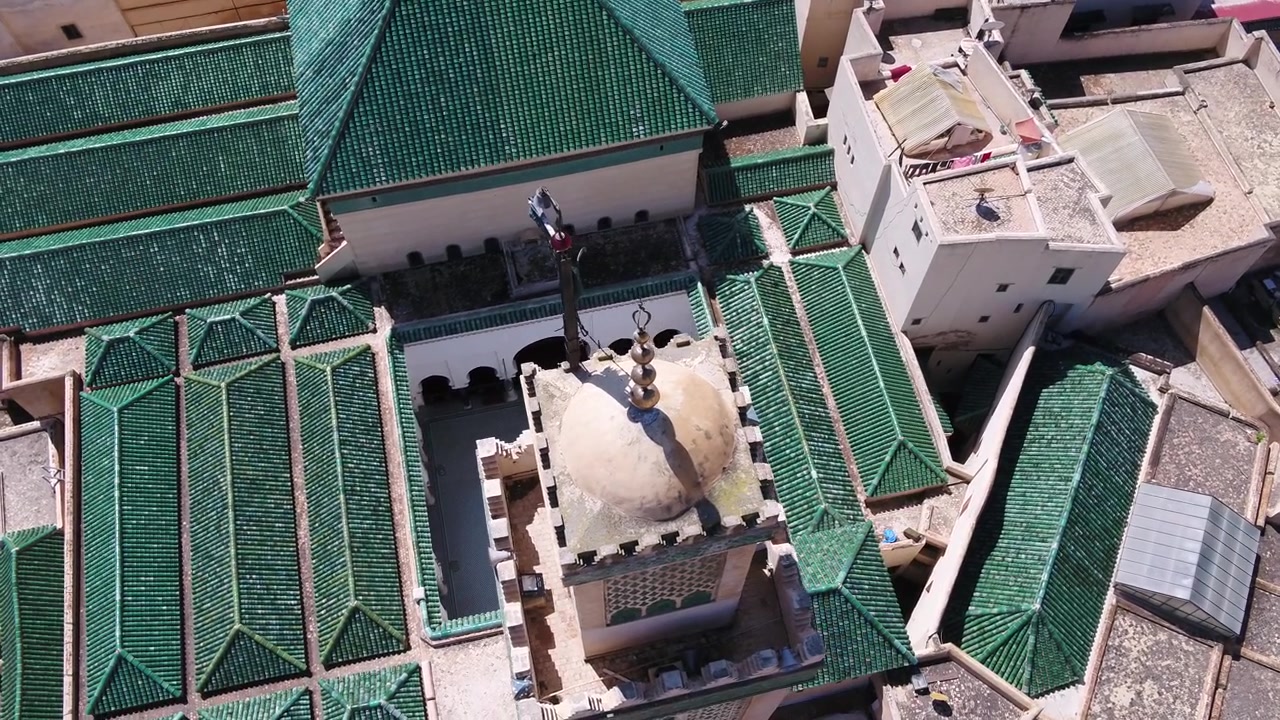Vista aerea con drone che cattura la storica cupola del minareto, il cortile interno ornato e i tetti a piramide con tegole verdi della Moschea Al Quaraouiyine a Fez, Marocco.