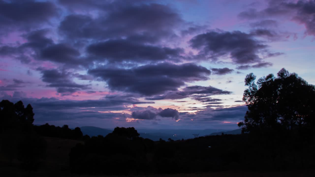 Time lapse at sunset with color full at a cloudy day with dark silhouette of trees and a big star appears, in Colombian fields