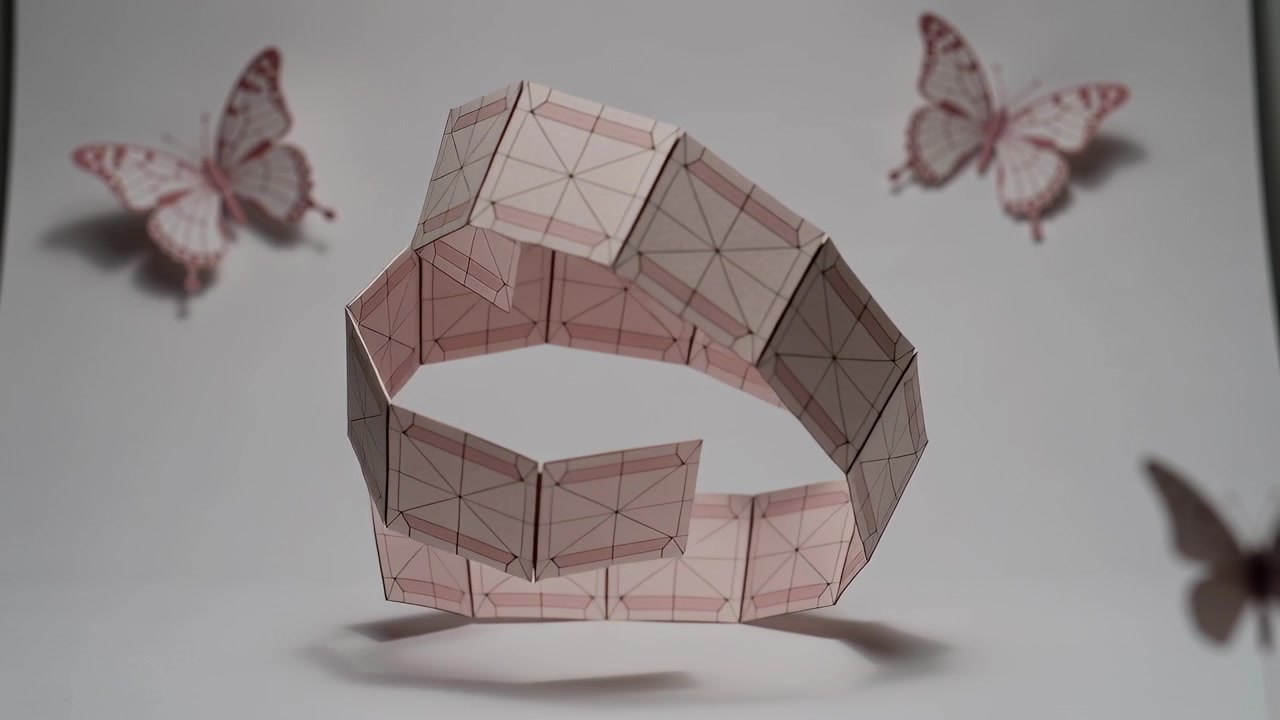 Unfolding modular pink paper panels with grid guides rotating in studio, reconfiguring to form ring