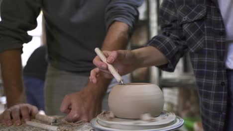 dos personas formando una olla de arcilla en una rueda de cerámica