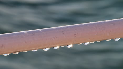 close up: dew drops on ship railing reflect spectral sunshine on water