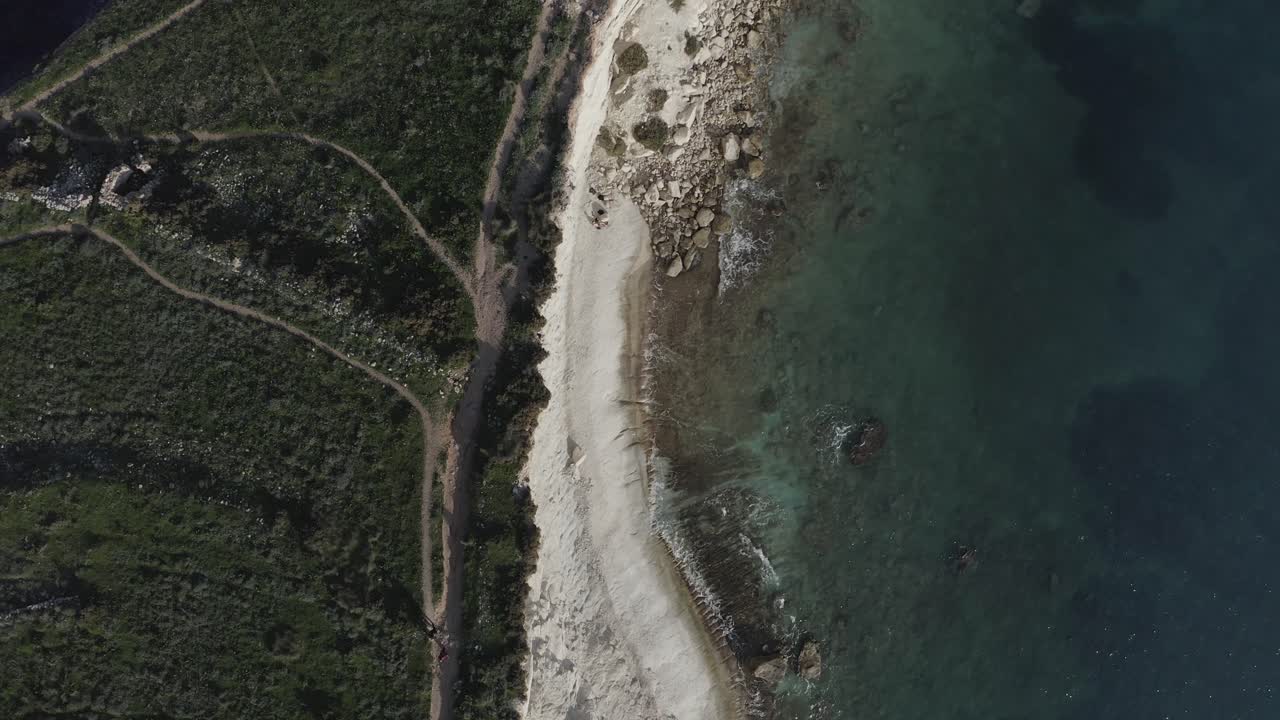 A drone flies above Ras il-Fenek’s rugged coast, with sheer limestone cliffs close to the camera and the distant blue sea, creating dramatic depth and perspective