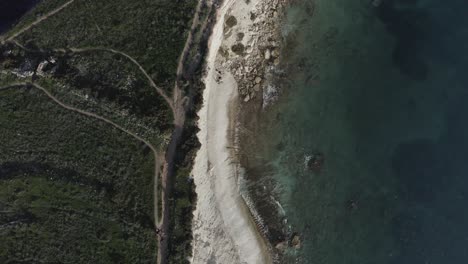 a drone flies above ras il-fenek’s rugged coast, with sheer limestone cliffs close to the camera and the distant blue sea, creating dramatic depth and perspective