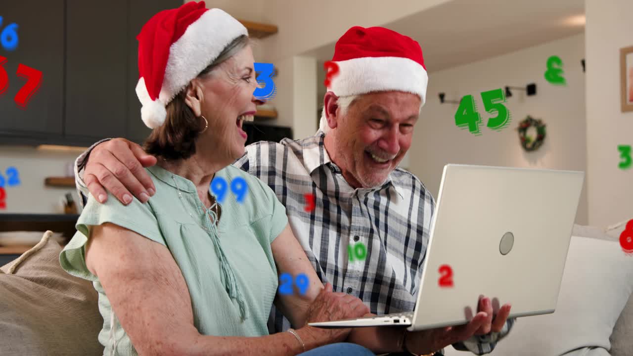 Senior couple in Santa hats on couch, woman typing laptop starting floating digits seeing sales