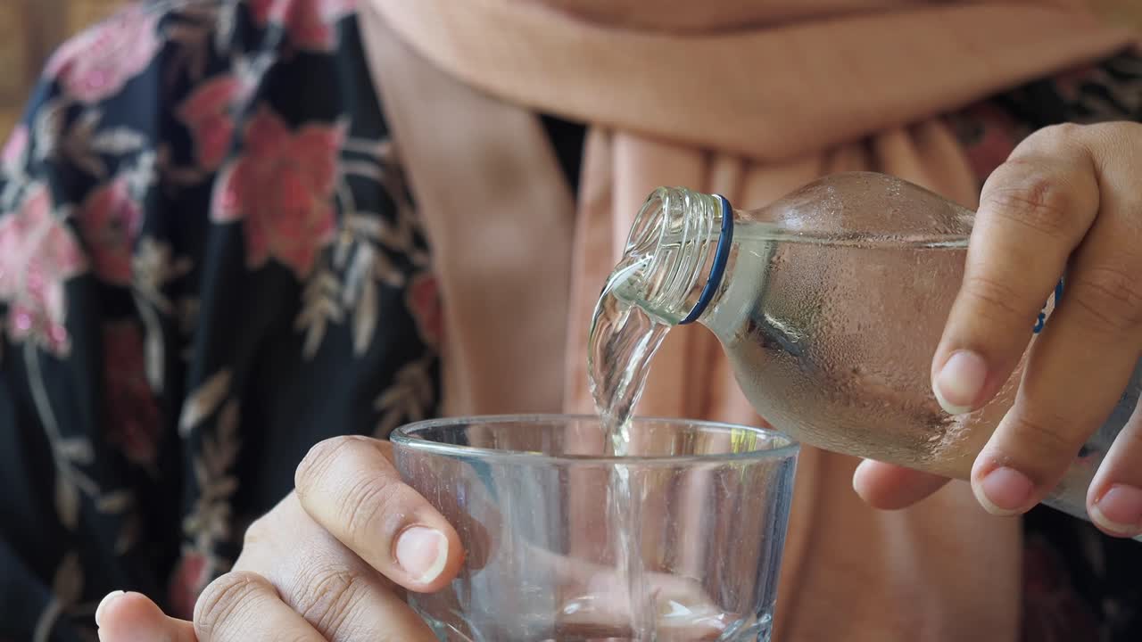 한 여자 가 병 에서 물 을 유리잔 에 부어 넣고 있다