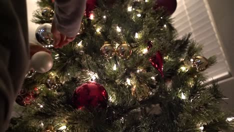 close-up of young boy's hands hooking on festive ornaments on a christmas tree