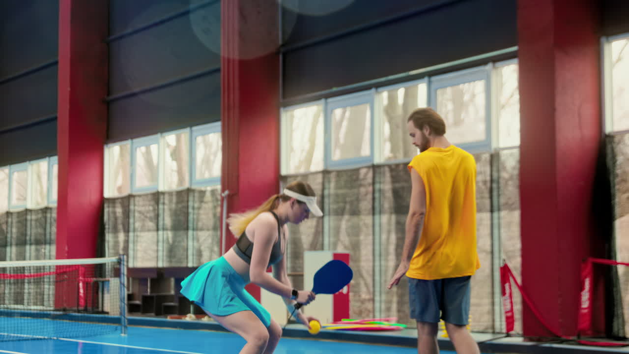 A man teaching a woman how to play pickleball in an inside court