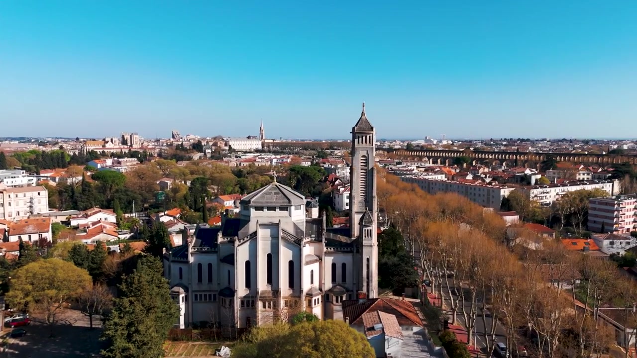 Drone buer til højre rundt om en kirke i La Rochelle ved siden af en lang træallé
