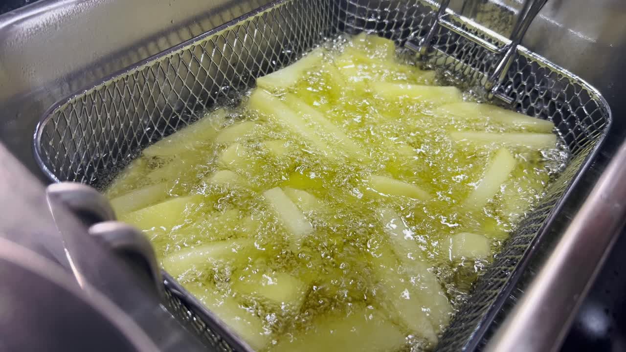 Skiveskårne kartofler, der syder i varm olivenolie i en frituregryde. Traditionel madlavning med boblende tekstur og gylden farve