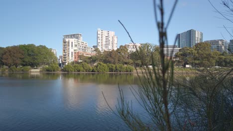 Schöner-Und-Ruhiger-Fluss-Am-Morgen-Mit-Wohngebäude-Am-Wasser-Im-Hintergrund