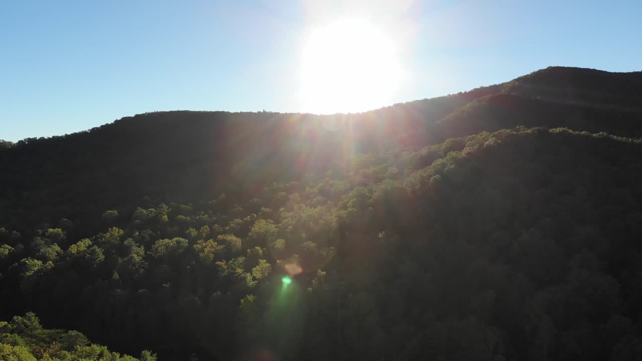 montañas boscosas al atardecer con llamaradas solares, disparo de seguimiento aéreo