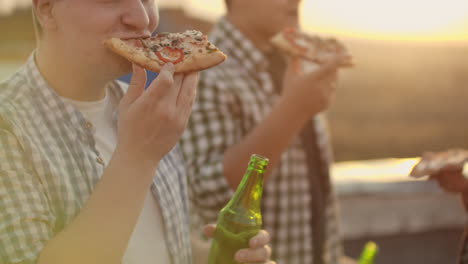 un hombre come un pedazo de pizza caliente y bebe cerveza en la fiesta con sus fritos.