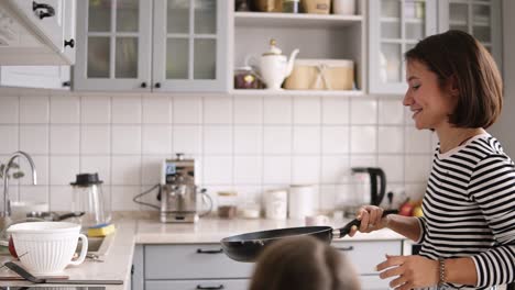 beautiful woman with short brown hair turns over pancakes in a frying pan and smile