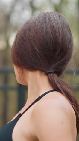 closeup of woman stretching neck in neck top near iron fence with blurred trees in background, highlighting flexibility, relaxation, and wellness in a natural outdoor setting