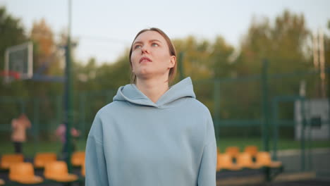 lady in blue hoodie serves volleyball with focus on her hand technique, blurred background of people in pink training outdoors, showing a sports practice session on a volleyball court