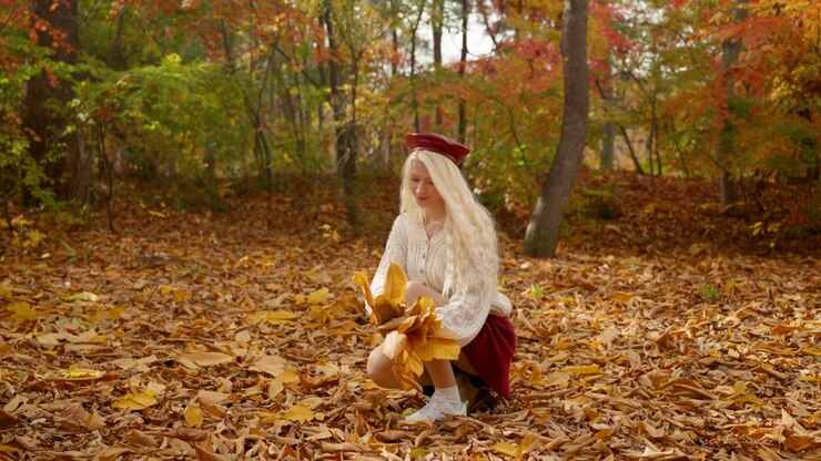 Europese vrouw in feestelijke kleding bukt om herfstbladeren te verzamelen in Forest Park, met een kleurrijke, warme achtergrond, statische opname in medium slow motion.