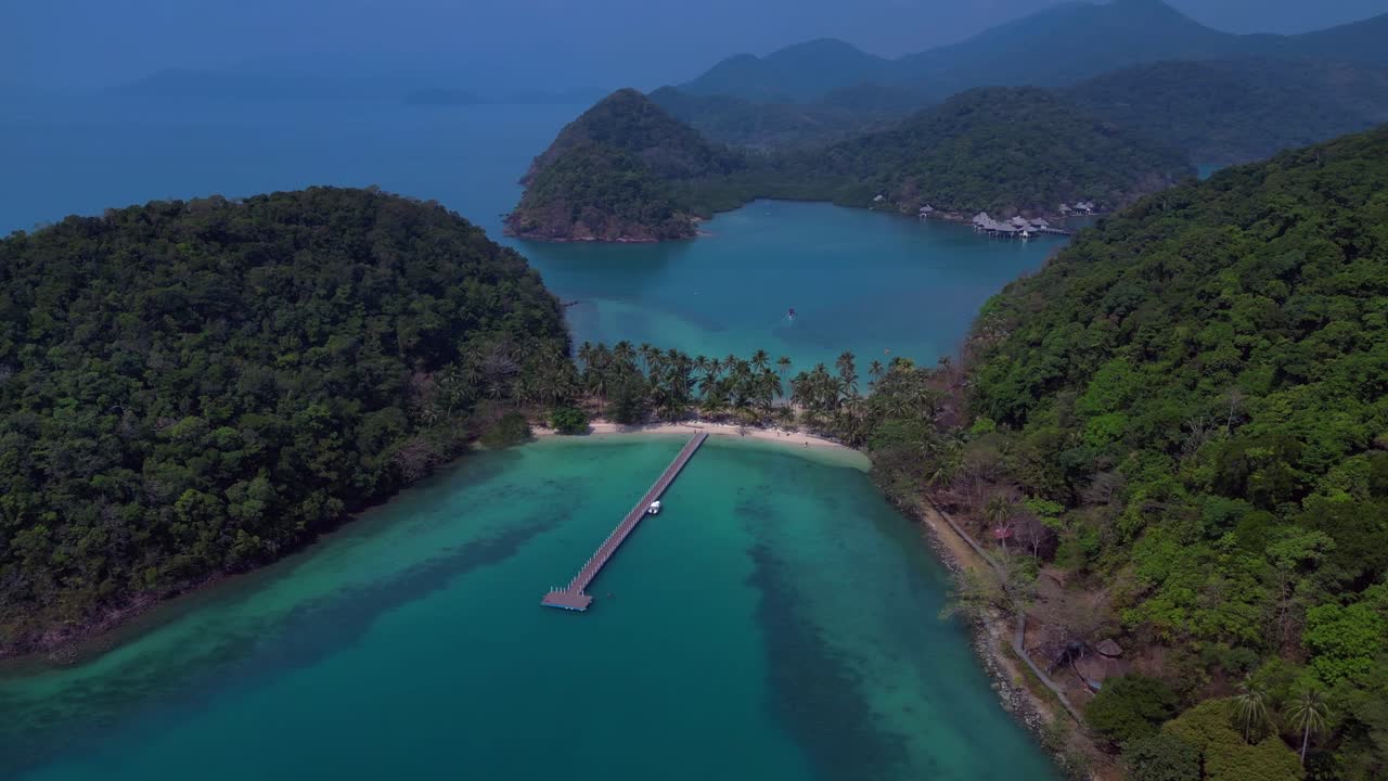 Koh Chang's idyllic landscape, featuring lush greenery, a pristine beach, and a tranquil pier extending into the turquoise waters. Gorgeous aerial view flight wide orbit overview drone