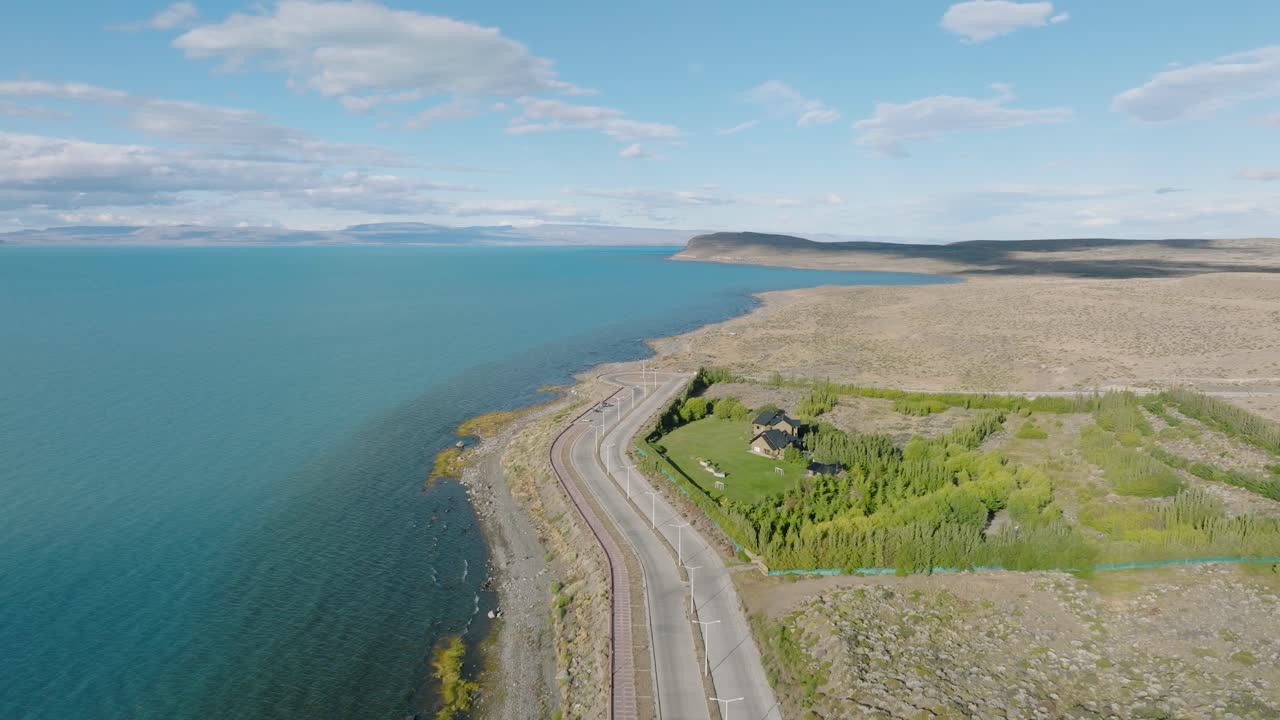 Aerial view of winding coastal road along turquoise Lago Argentino near El Calafate, Argentina. Dramatic Patagonian landscape, pristine highway cutting through hills.