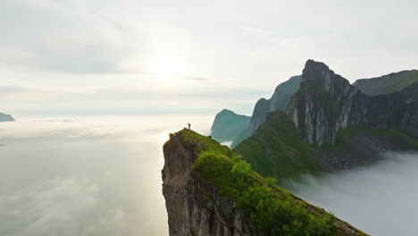 female hiker climb arctic senja hesten mountain ridge in sunlight glow; drone