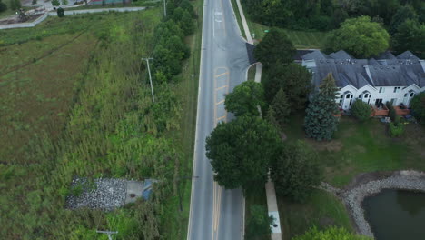 Elevated-aerial-drone-footage-following-a-street-through-a-scenic-lush-suburban-neighborhood-landscape-of-middle-class-America