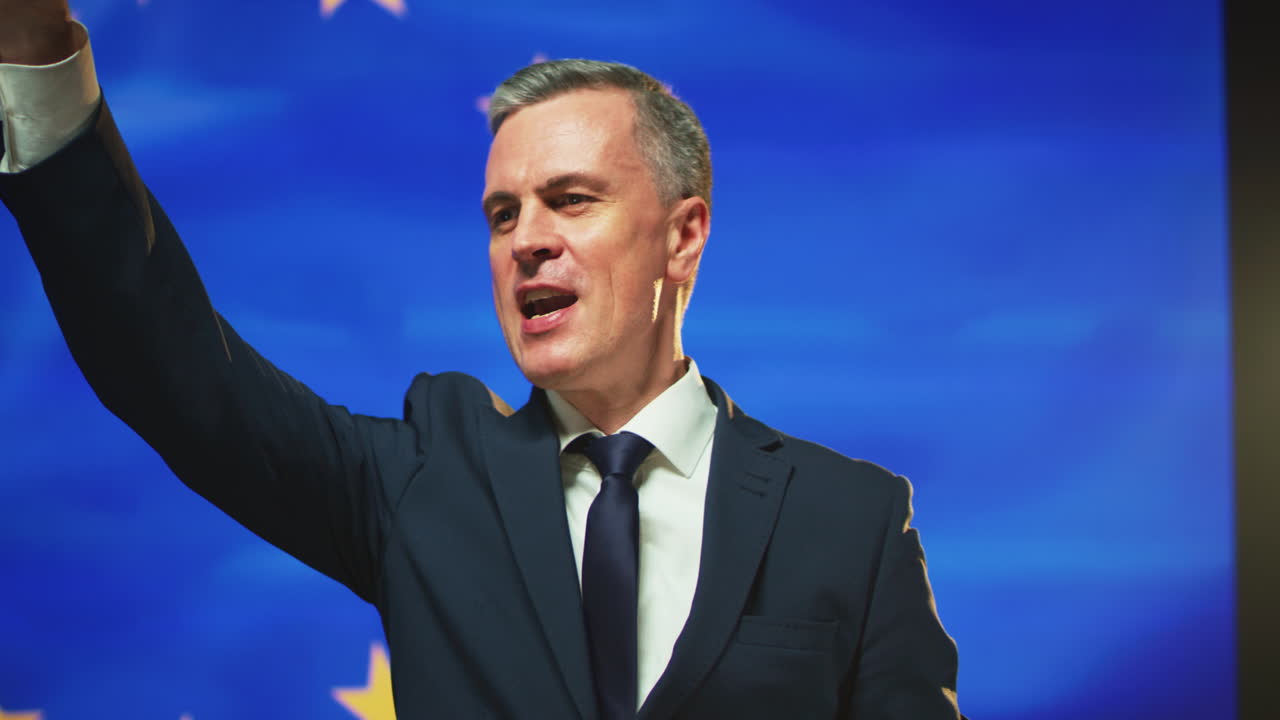 Successful Politician Giving Promises against European Flag Pan around View of Man in Suit Gesticulating and Persuading Audience during Speech against Flag of Europe on Stage
