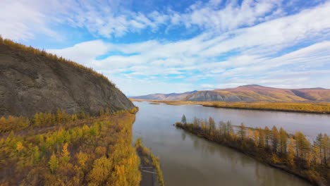 breathtaking views capture the tranquil beauty of a river winding through golden foliage, framed by majestic mountains under a bright, blue sky during the captivating autumn season.