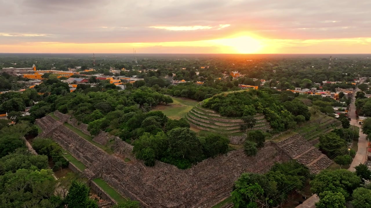 Panorama aereo al tramonto sulla città di Izamal, Yucatan, Messico, con le strade coloniali e la foresta che brillano sotto un cielo serale ambrato.