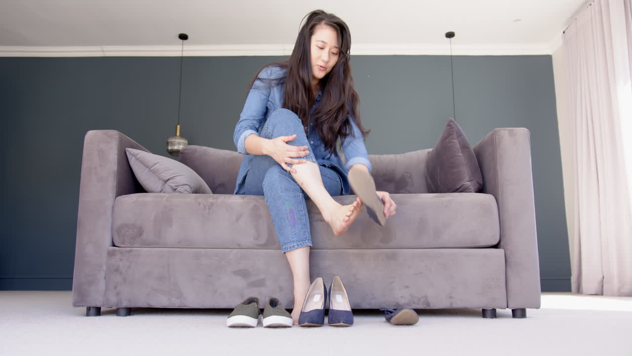 Trying on shoes, woman sitting on couch and adjusting footwear in living room