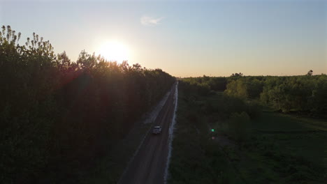 white pickup truck driving along a long dirt road, surrounded by lush green forest, capturing the stunning hues of sunset, viewed from above