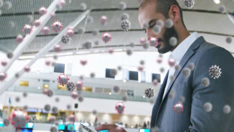 animation of floating covid-19 cells over mixed race man using smartphone at airport