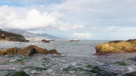 Waves-crashing-at-rocks-with-algae-on-a-cloudy-day