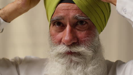 fotografía de estudio de cerca de un anciano sikh con barba usando la aguja salai al ponerse el turbante contra un fondo plano 4