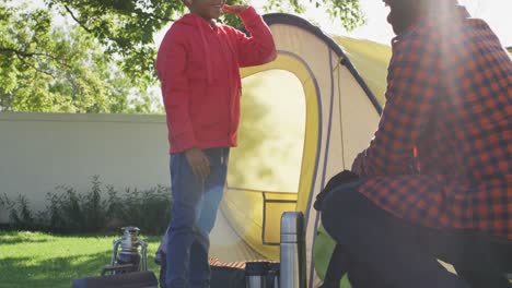 happy african american father and his son setting up tent and high-fiving in garden