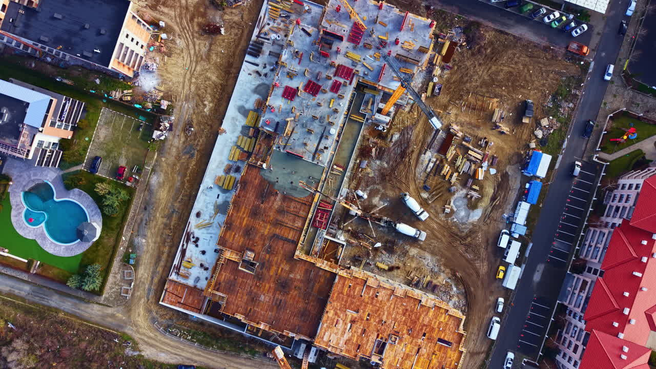 Fortschritt auf der Baustelle eines großen Gebäudes mit Kränen, LKWs und Materialien in einem städtischen Gebiet während der Tagesstunden