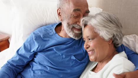 Happy-senior-biracial-couple-lying-on-bed-and-embracing,-unaltered,-in-slow-motion