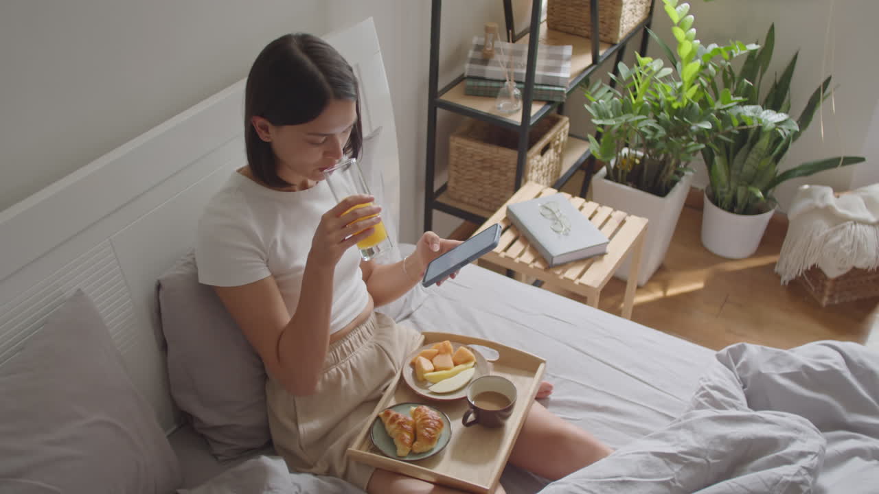 Woman Using Cell Phone and Having Breakfast in Bed
