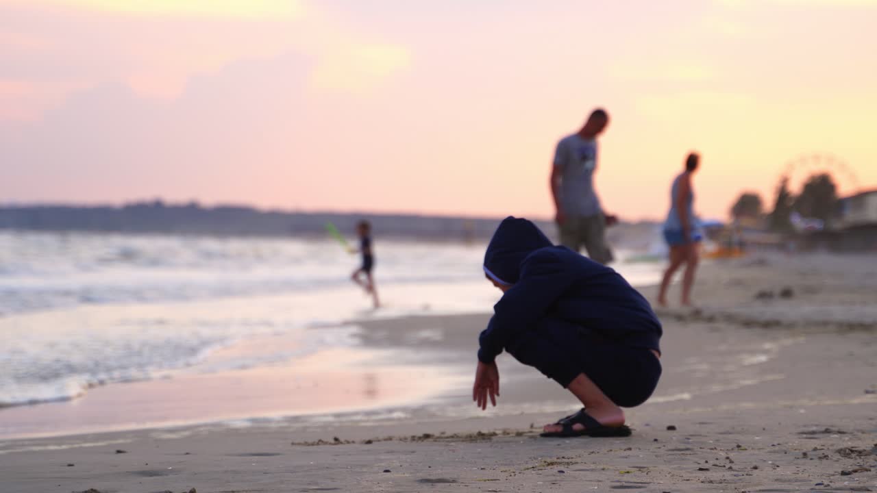 Boy sitting on beach. Outdoor view of young boy drawing in sand on natural sea background