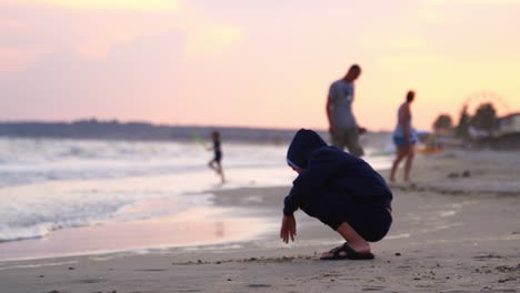 boy sitting on beach. outdoor view of young boy drawing in sand on natural sea background