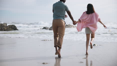 couple running on a sandy beach holding hands