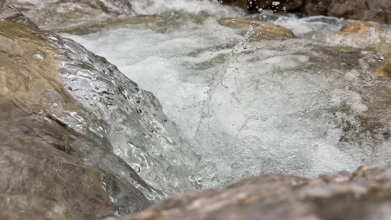 Primo piano dettagliato dell'acqua limpida del fiume che scorre su rocce levigate, creando schiuma, bolle e texture vorticose