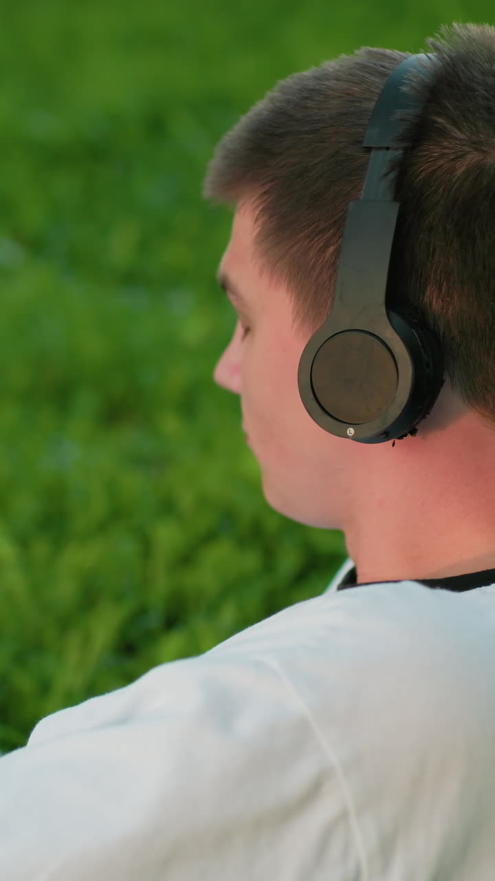 Man lies on his side in grassy field enjoying music outdoors, resting on his hand with headphones, looking relaxed and content in a peaceful natural environment