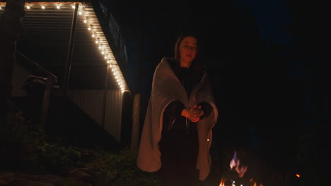 mujer frotando las manos sobre el fuego tarde en la noche. mujer joven toma un paseo dentro de los terrenos de la morada de acampada navegando patio en busca de calor